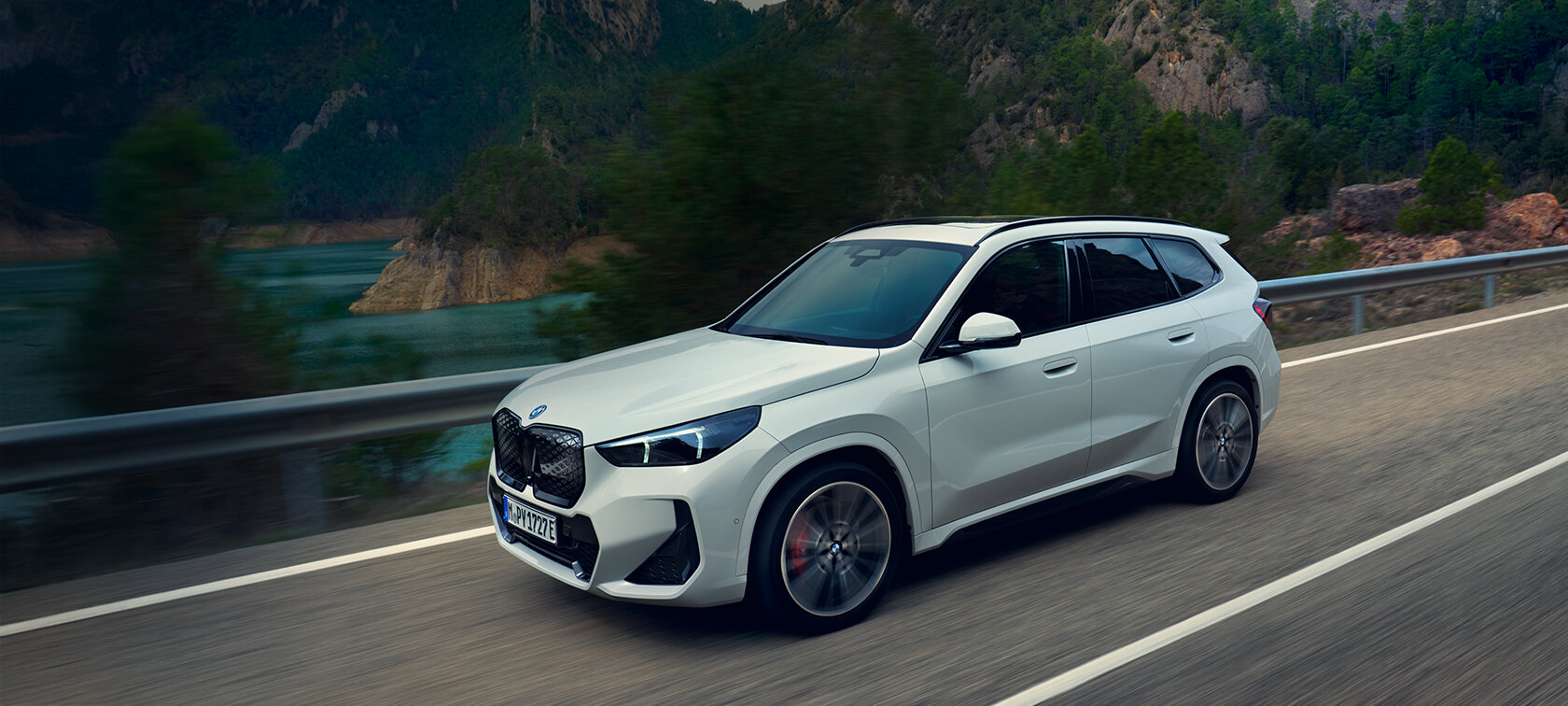Weißer BMW iX1 xDrive30 mit M Sportpaket fahrend auf einer Landstraße - Angebot für Großkunden bei der Wahl-Group