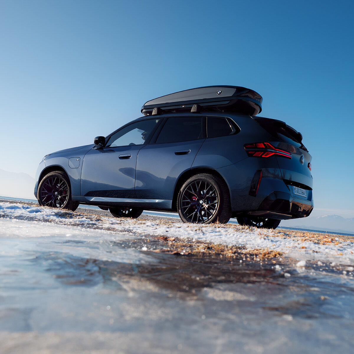 BMW X3 30e mit Winterkompletträder | Original BMW Winterräder Original BMW X3 30e xDrive (G45) als PHEV mit sportlichen, schwarzen Winterkompletträdern und Dachbox in winterlicher Schneelandschaft.