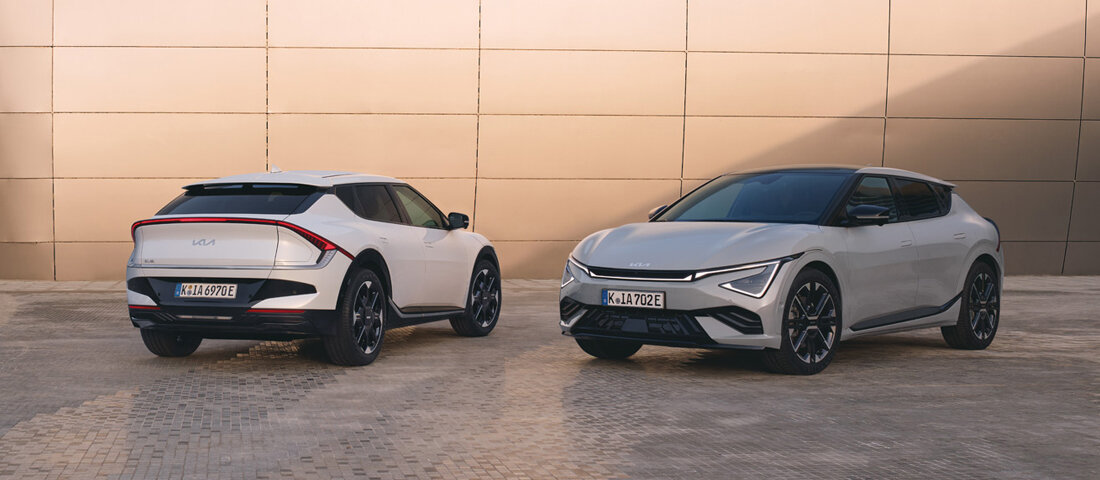 Kia EV6 2024 Modell in Snow White Pearl und Interstellar Gray | Vorder- und Heckansicht Zwei Kia EV6 2024 Modelle in kontrastierenden Posen vor goldfarbener Wand - ein weißes Modell von hinten und ein graues Modell von vorne. Beide Fahrzeuge zeigen das charakteristische LED-Lichtdesign und die dynamische Crossover-Silhouette.