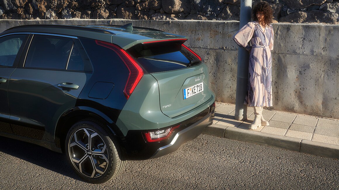 Kia Niro Heckansicht – Elegantes Design und klare Linienführung Heckansicht des Kia Niro mit Frau, die an einer Laterne steht, im Hintergrund