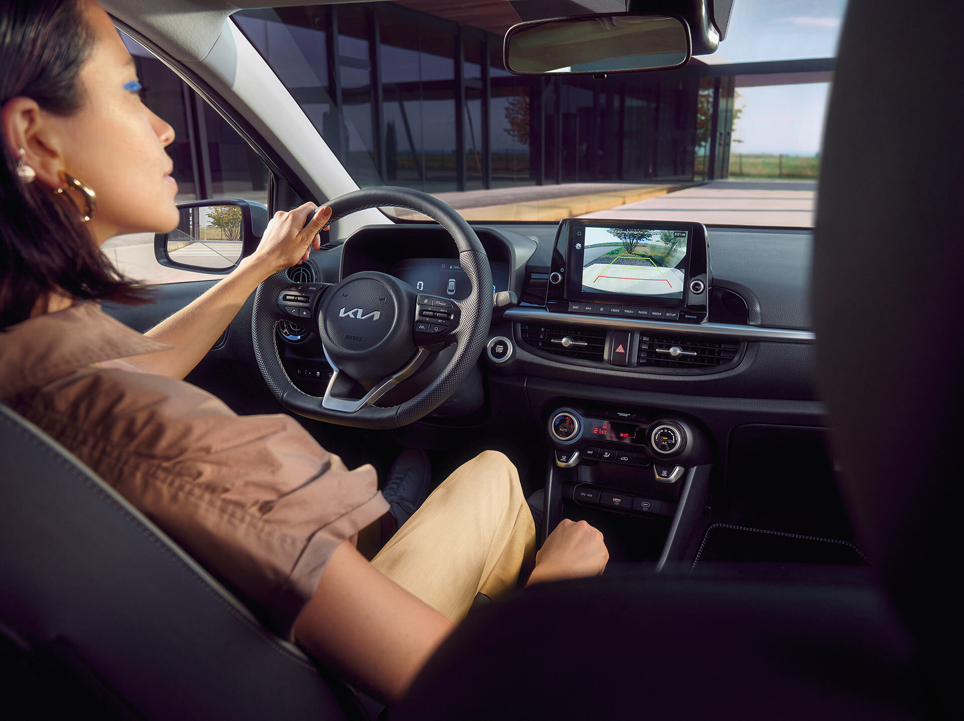 Fahrerinnenperspektive des Kia Picanto Cockpits mit Multifunktionslenkrad, digitalem Display und Rückfahrkamera-Ansicht auf dem zentralen 8-Zoll Touchscreen