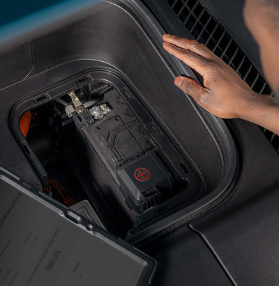 Hand an der geöffneten Abdeckung der Starterbatterie in einem Kia