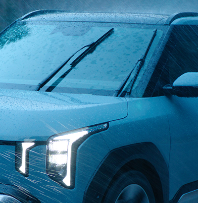 Front eines Kia EV2 mit eingeschalteten Scheinwerfern und Wischerblättern im Regen