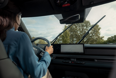 Fahrerin im Kia bei Regen, die Scheibenwischer laufen über die Windschutzscheibe